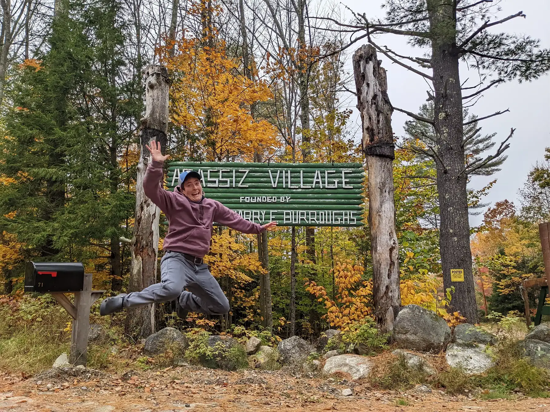 A camper jumping in the air in front of the Agassiz Village sign